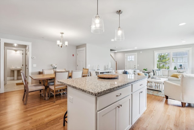 kitchen with a notable chandelier, a center island, light wood-style flooring, white cabinets, and open floor plan