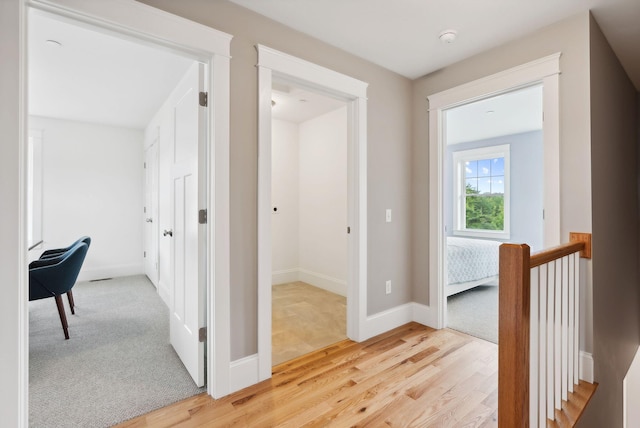 hall with an upstairs landing, light wood-style flooring, and baseboards