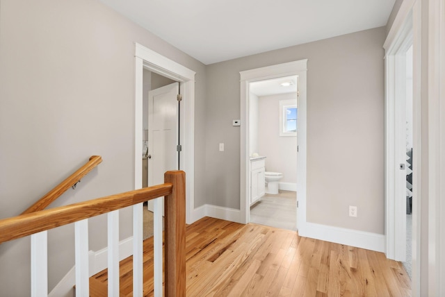 hallway with an upstairs landing, light wood-style floors, and baseboards