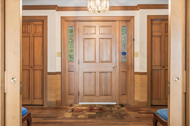 entrance foyer featuring ornamental molding, an inviting chandelier, wainscoting, and dark wood finished floors