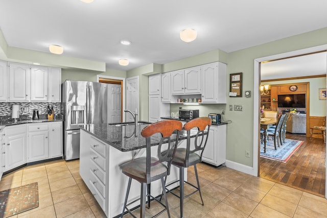 kitchen with dark stone countertops, light tile patterned floors, stainless steel fridge with ice dispenser, a kitchen bar, and a sink
