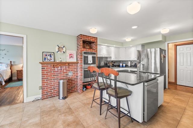 kitchen with decorative backsplash, light tile patterned floors, a kitchen bar, white cabinets, and appliances with stainless steel finishes