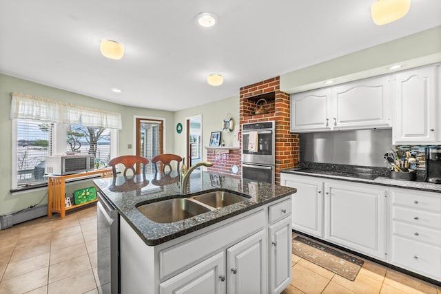 kitchen featuring a kitchen island with sink, a sink, light tile patterned floors, white cabinets, and appliances with stainless steel finishes
