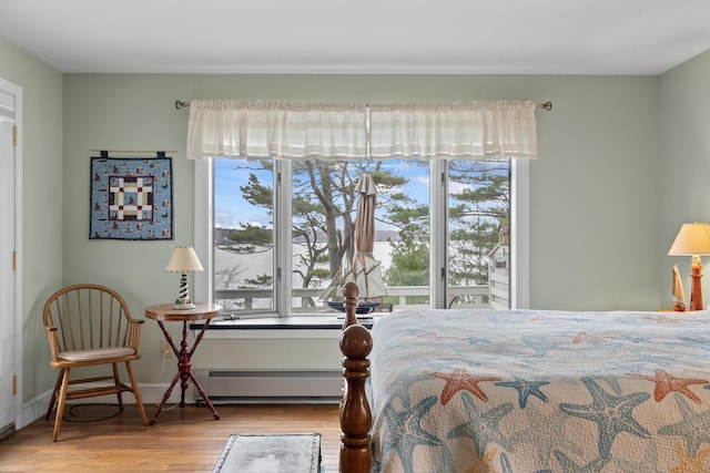 bedroom featuring wood finished floors, baseboards, baseboard heating, and multiple windows