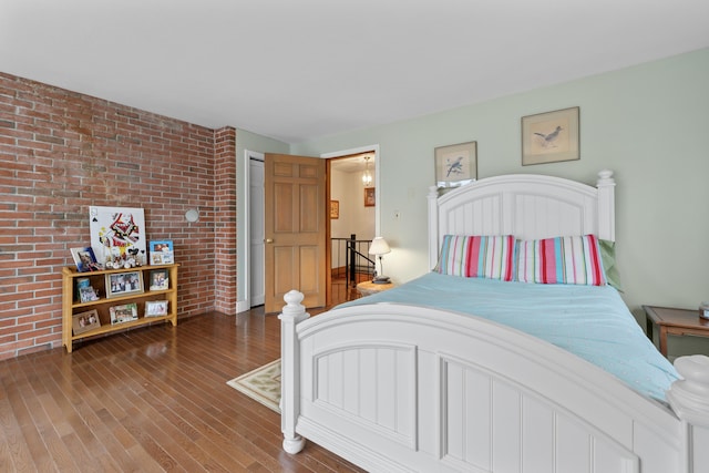 bedroom with wood finished floors and brick wall