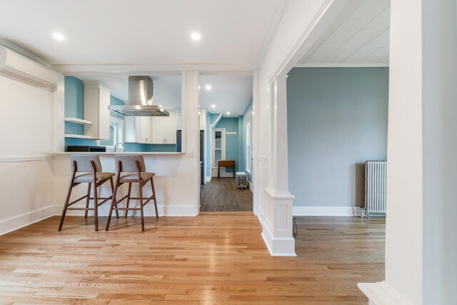 32 Webster Ave, Bangor, ME 04401 - kitchen featuring a breakfast bar area, white cabinetry, light wood-style floors, radiator, and island exhaust hood