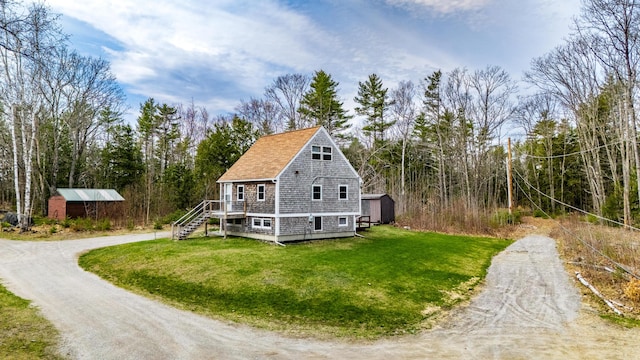 view of side of property featuring driveway, an outdoor structure, stairs, a storage unit, and a yard
