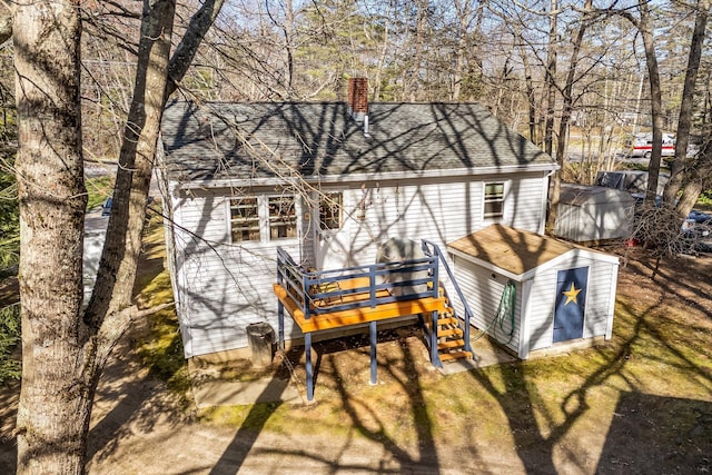 back of house featuring a shed, an outdoor structure, a wooden deck, roof with shingles, and a chimney