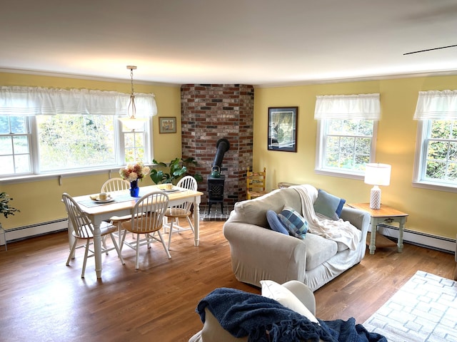 living room featuring wood finished floors, crown molding, a wood stove, and a baseboard heating unit