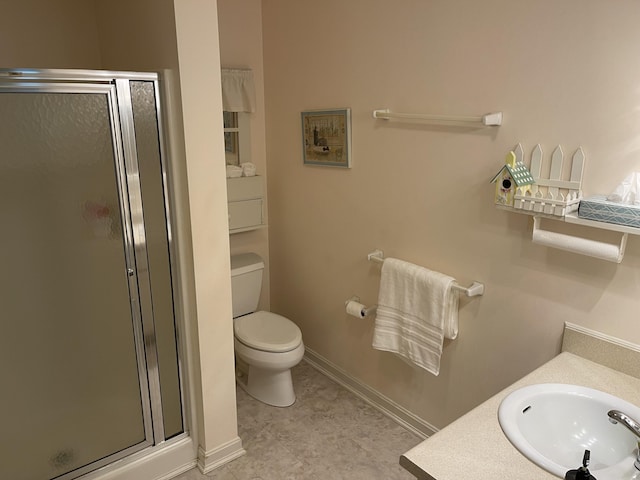 bathroom with toilet, vanity, a shower stall, and baseboards