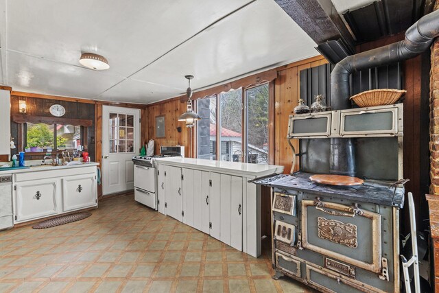 kitchen featuring light floors, white gas range oven, wood walls, dishwasher, and white cabinetry