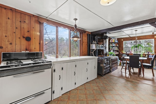 kitchen featuring wood walls, white gas stove, light floors, and white cabinets