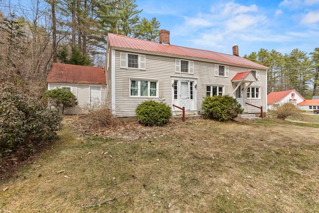 colonial house with a chimney, a front yard, and metal roof