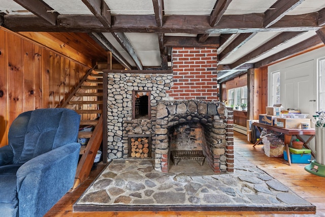 living area featuring beamed ceiling, a fireplace with raised hearth, wood walls, hardwood / wood-style flooring, and a baseboard radiator