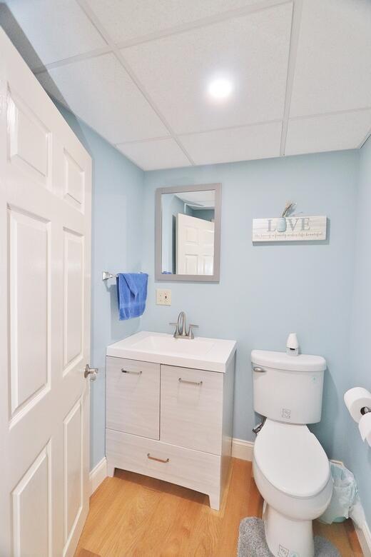 half bath with vanity, toilet, a paneled ceiling, baseboards, and wood finished floors