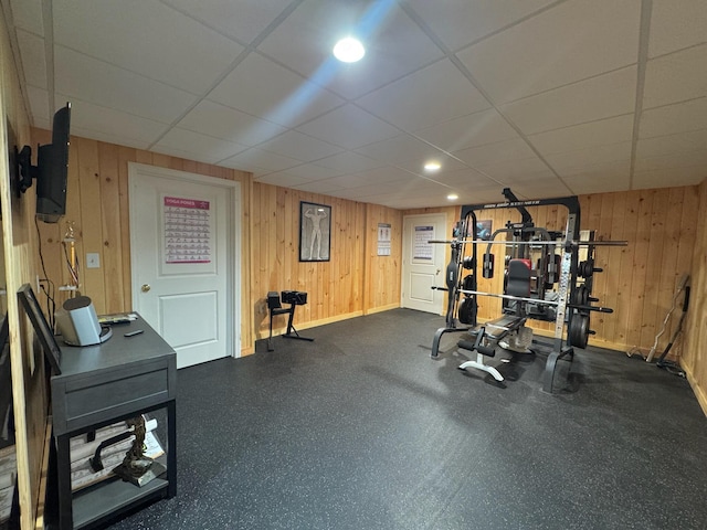 workout area with baseboards, wood walls, and a drop ceiling