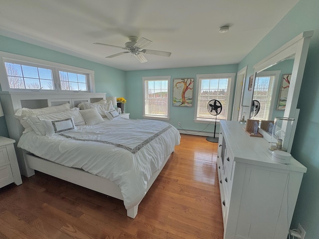 bedroom featuring a ceiling fan, wood finished floors, and baseboard heating