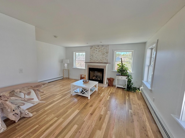 living area with baseboards, a baseboard radiator, light wood finished floors, and a large fireplace