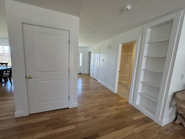 hallway featuring built in shelves, baseboards, and wood finished floors