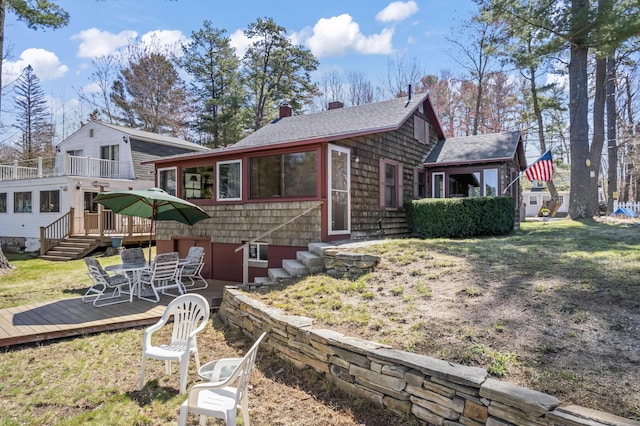 view of front facade with a front lawn, roof with shingles, a wooden deck, and a chimney