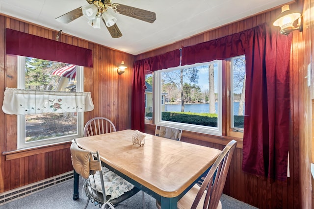 dining room featuring a water view, carpet, a ceiling fan, and wood walls