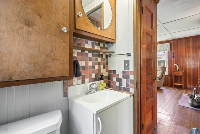 bathroom featuring vanity, toilet, wood walls, hardwood / wood-style floors, and tasteful backsplash
