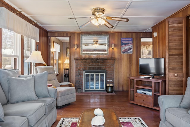 living room featuring wooden walls, ceiling fan, a brick fireplace, and wood finished floors