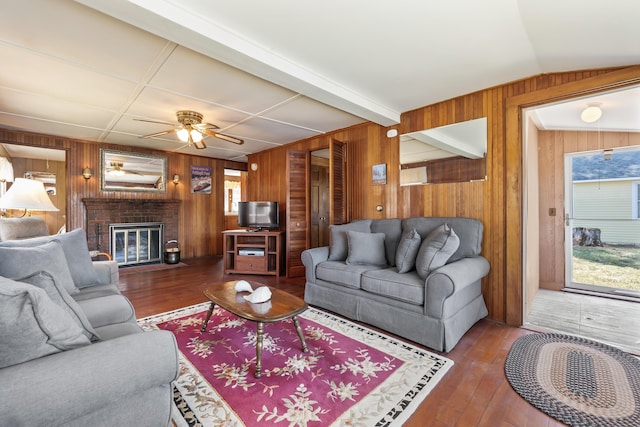 living area featuring wooden walls, ceiling fan, a brick fireplace, and hardwood / wood-style floors