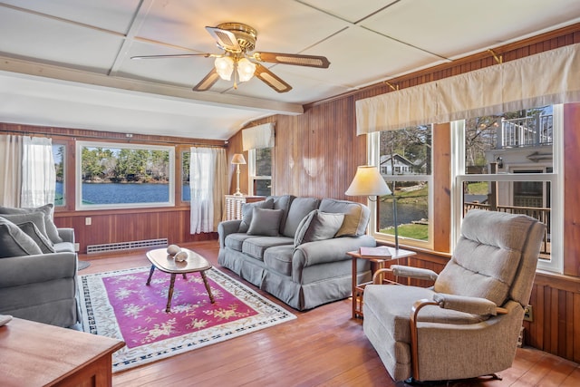 living room featuring wooden walls, plenty of natural light, a baseboard radiator, and ceiling fan