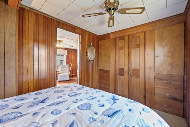 carpeted bedroom with wooden walls, a ceiling fan, and a closet