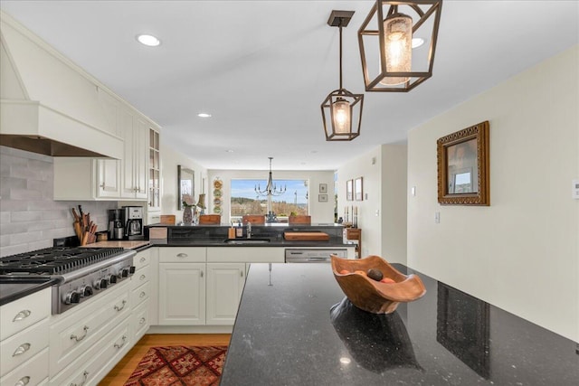 kitchen featuring a sink, stainless steel gas cooktop, a peninsula, backsplash, and pendant lighting
