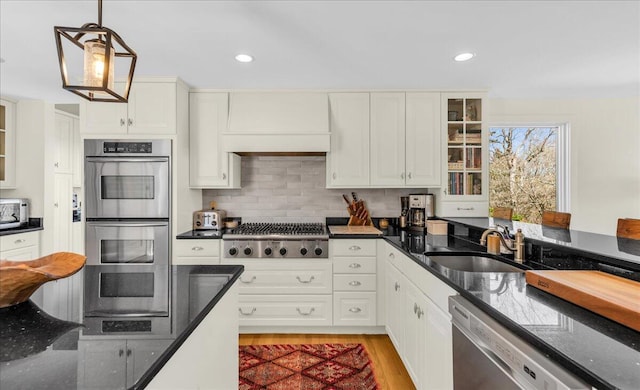 kitchen with glass insert cabinets, light wood-style floors, a sink, appliances with stainless steel finishes, and hanging light fixtures