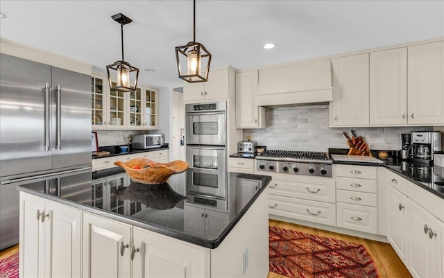 kitchen with appliances with stainless steel finishes, light wood finished floors, a center island, tasteful backsplash, and glass insert cabinets