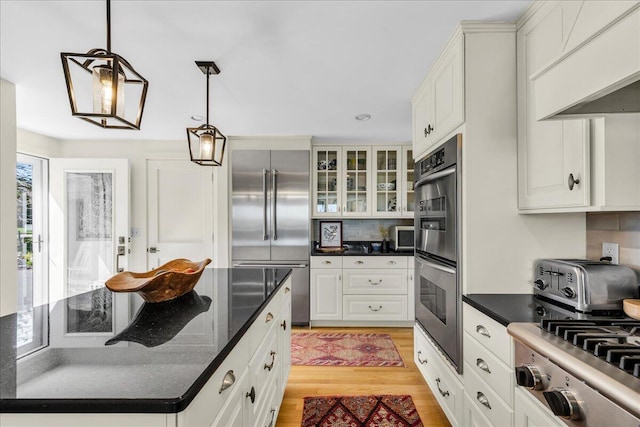 kitchen with light wood-style flooring, stainless steel appliances, a toaster, pendant lighting, and glass insert cabinets