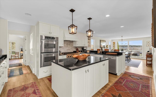 kitchen featuring a peninsula, dark countertops, a center island, light wood-style flooring, and appliances with stainless steel finishes