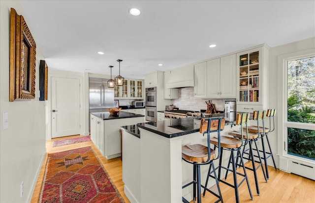 kitchen with dark countertops, stainless steel double oven, light wood-style floors, and a center island