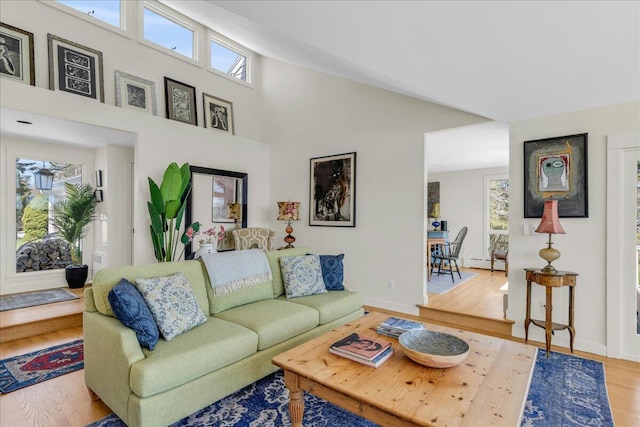 living area with a baseboard heating unit, a wealth of natural light, and wood finished floors