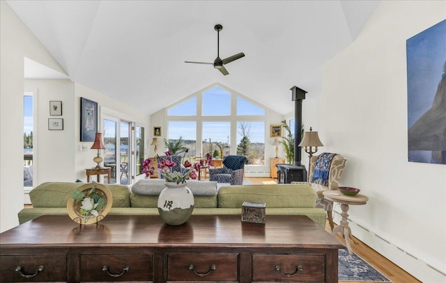living area featuring ceiling fan, baseboard heating, a wood stove, vaulted ceiling, and wood finished floors