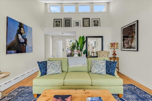 living area with a towering ceiling, baseboards, baseboard heating, and wood finished floors
