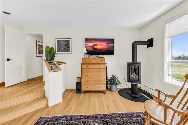 sitting room with baseboards, a wood stove, and wood finished floors