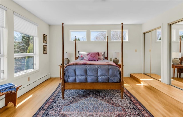 bedroom featuring baseboards, multiple closets, wood finished floors, and baseboard heating