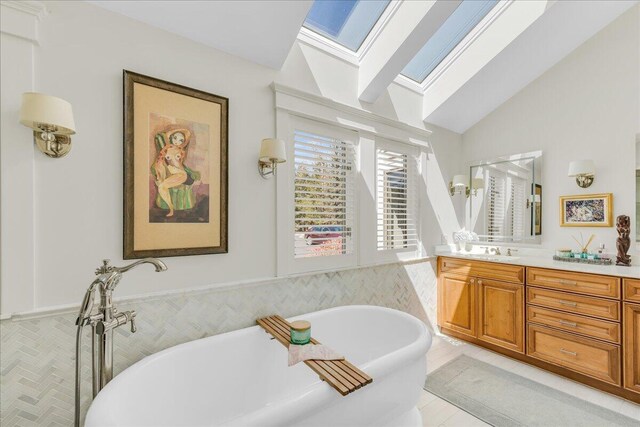 full bathroom with vaulted ceiling with skylight, vanity, and a freestanding bath