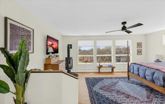 bedroom with baseboard heating, a wood stove, and wood finished floors