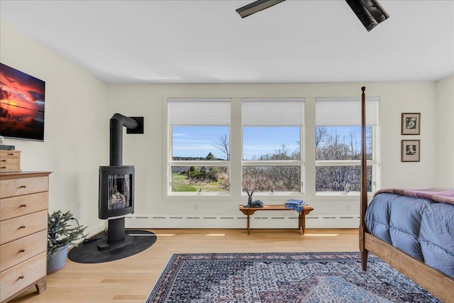 bedroom with multiple windows, a wood stove, and wood finished floors
