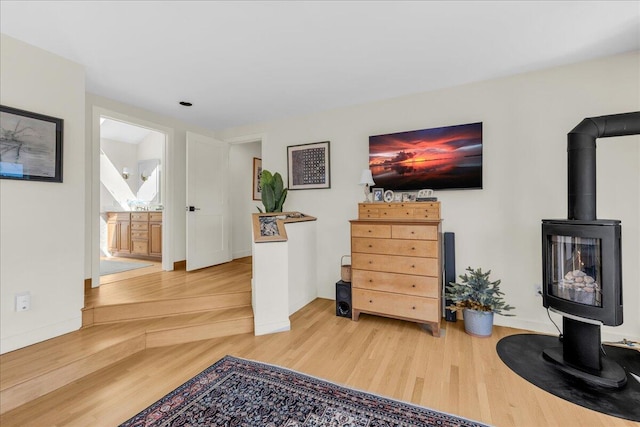 living area with baseboards, a wood stove, and light wood-style flooring