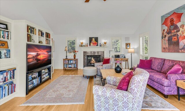 living room with a healthy amount of sunlight, a high end fireplace, vaulted ceiling, and wood finished floors