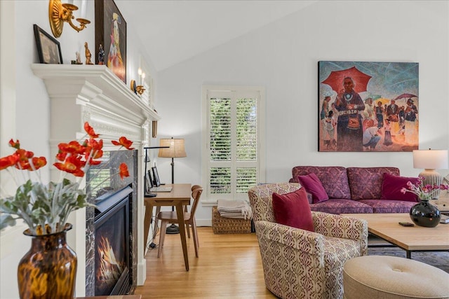 living room featuring light wood-style flooring, lofted ceiling, and a warm lit fireplace