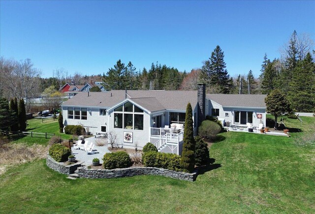 rear view of house with a lawn, a sunroom, a chimney, and a patio area