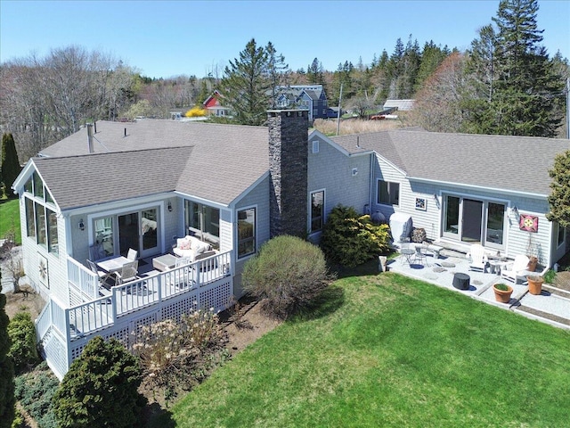 back of property featuring a deck, a patio, a chimney, a shingled roof, and a yard