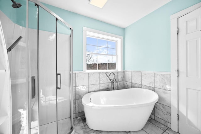bathroom featuring a stall shower, tile walls, marble finish floor, a soaking tub, and a wainscoted wall